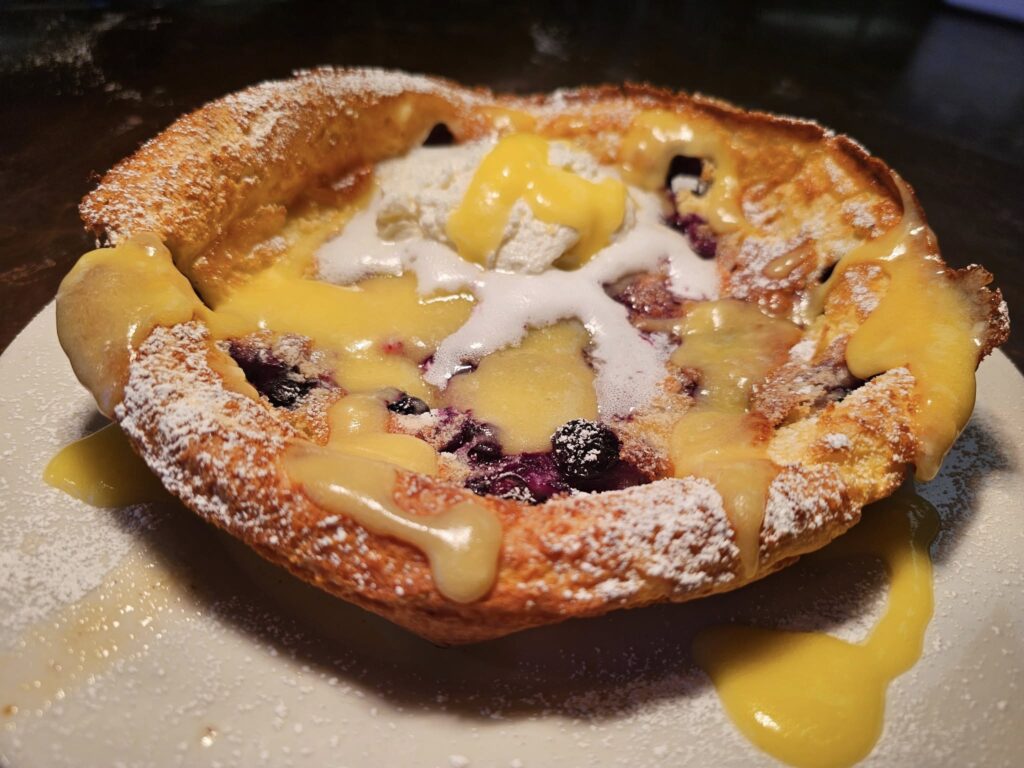 A decadent dish featuring a golden brown crust with lemon and blueberry filling topped with powdered sugar.