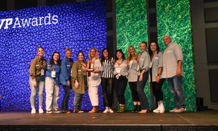 A group of 11 people stands on a stage holding an Award in front of a blue background that says "MVP Awards."